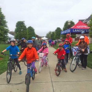 Children riding bicycles and wearing bicycle helmets donated by Breakstone, White & Gluck of Boston.