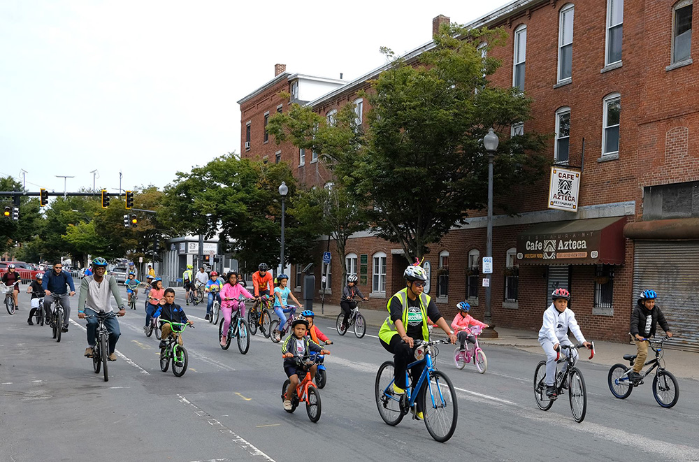 Cyclists riding and wearing bicycle helmets at the Lawrence Ciclovia. Breakstone, White & Gluck, a Boston personal injury law firm, donated helmets from its Project KidSafe campaign.