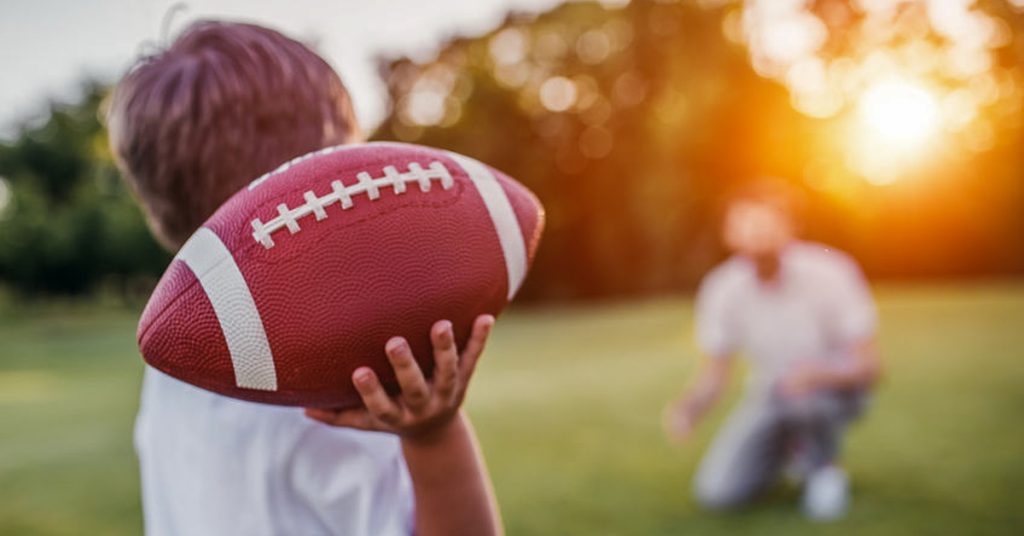Child in Boston throwing football to father in backyard.
