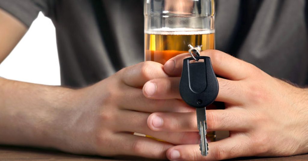 Teenager drinking beer and holding a car key, contemplating the dangerous idea of driving