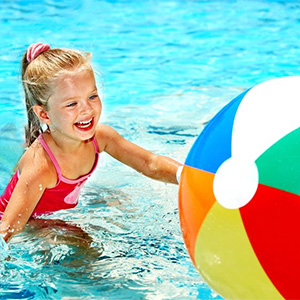 Young girl playing in a swimming pool with a beach ball.