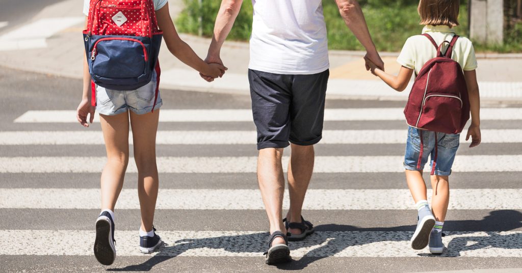 Two students walking to school in Boston, holding hands with their parent.