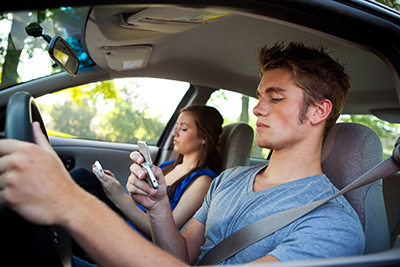 Teen driver and teen passenger sitting in front seat of car, using cell phones.